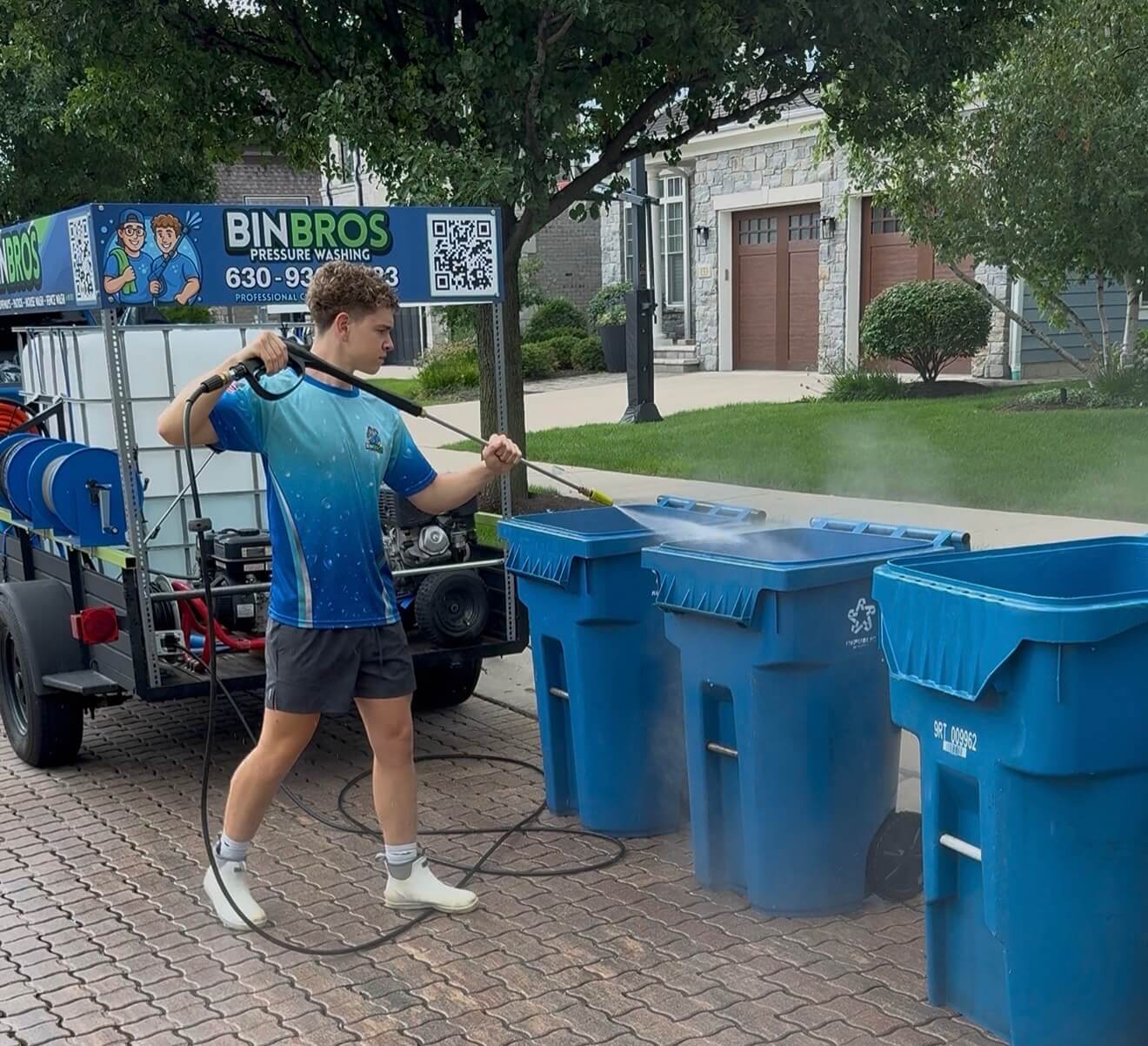 Bin Bros technician applying pest prevention spray to blue garbage and recycling cans beside the Bin Bros cleaning trailer in Elmhurst, Illinois